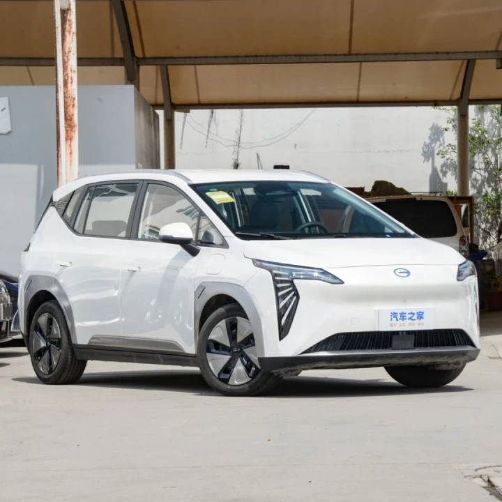 Un SUV eléctrico de color blanco brillante de la marca GAC, modelo Aion Y, estacionado bajo una estructura techada. El vehículo tiene un diseño moderno y aerodinámico, con ruedas aerodinámicas negras y detalles cromados. Se puede ver texto en chino en el lateral del vehículo. El auto tiene un aspecto futurista con líneas limpias y una parrilla distintiva.
